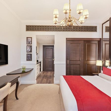 Dukes The Palm, A Royal Hideaway Hotel Dubai Exterior photo The photo shows a well-decorated hotel room. It features a large bed with a red and white color scheme, complemented by stylish pillows and a tufted headboard. A modern chandelier hangs from the ceiling, providing light. There is a flat-screen TV mou