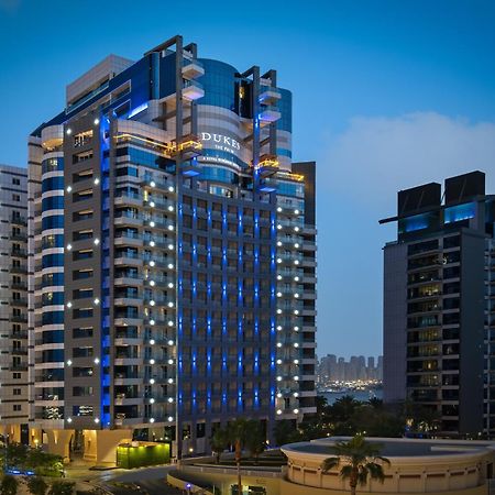 Dukes The Palm, A Royal Hideaway Hotel Dubai Exterior photo The photo shows a modern high-rise building, which appears to be a hotel or residential complex. The design features sleek lines and a glass façade, illuminated with blue lighting that enhances its contemporary look. Surrounding the main building are