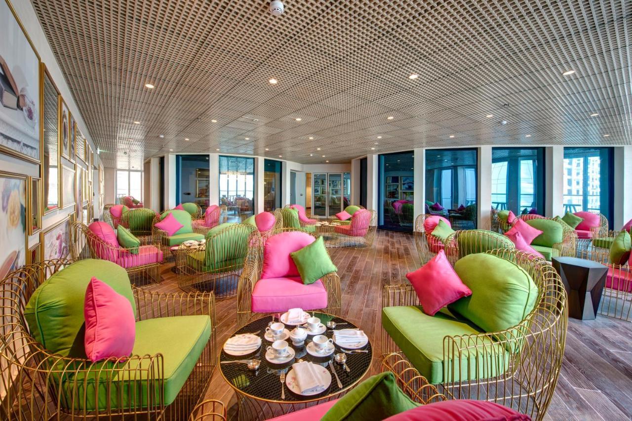Dukes The Palm, A Royal Hideaway Hotel Dubai Exterior photo The photo shows a stylish and modern lounge area. The seating consists of unique chairs and sofas that combine bright green and pink colors, adorned with matching cushions. The space has a contemporary design, featuring a wooden floor and large windo