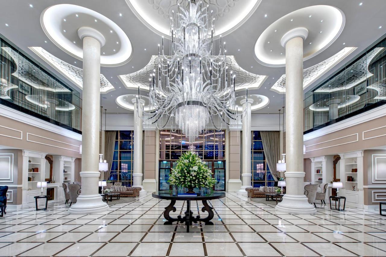 Dukes The Palm, A Royal Hideaway Hotel Dubai Exterior photo The photo depicts the interior of a luxurious lobby or hotel entrance. It features tall, elegant columns and a grand chandelier hanging from the ceiling, illuminating the space with soft light. The floor is tiled with a geometric pattern, enhancing t
