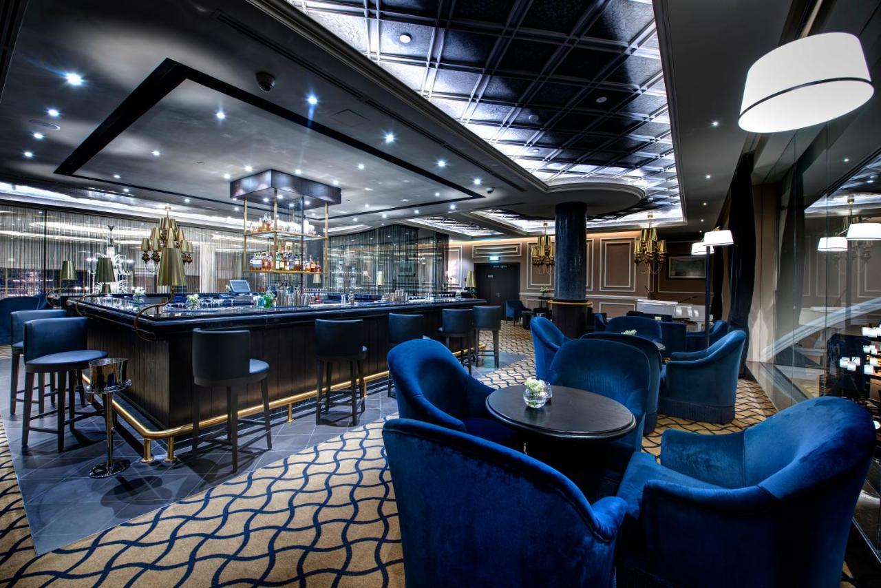 Dukes The Palm, A Royal Hideaway Hotel Dubai Exterior photo The photo shows an upscale bar or lounge area. The interior features modern design elements with elegant lighting. There is a stylish bar counter with a variety of drinks, and seating consists of plush blue armchairs arranged around small tables. The