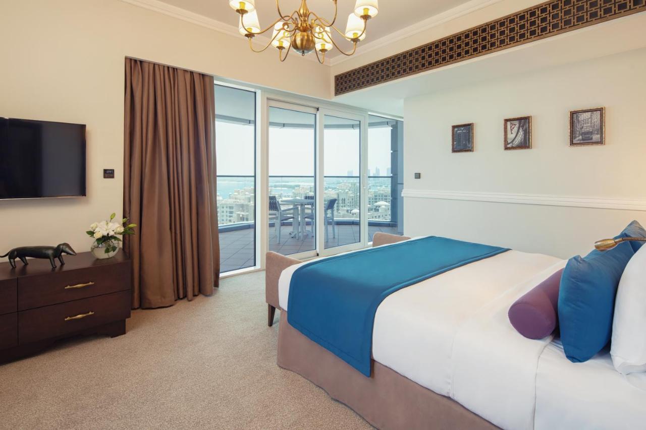 Dukes The Palm, A Royal Hideaway Hotel Dubai Exterior photo The photo shows a stylish and modern bedroom. It features a large bed with a blue and purple throw blanket, complemented by decorative pillows. Next to the bed, there is a dark wooden nightstand. A flat-screen TV is mounted on the wall opposite the b