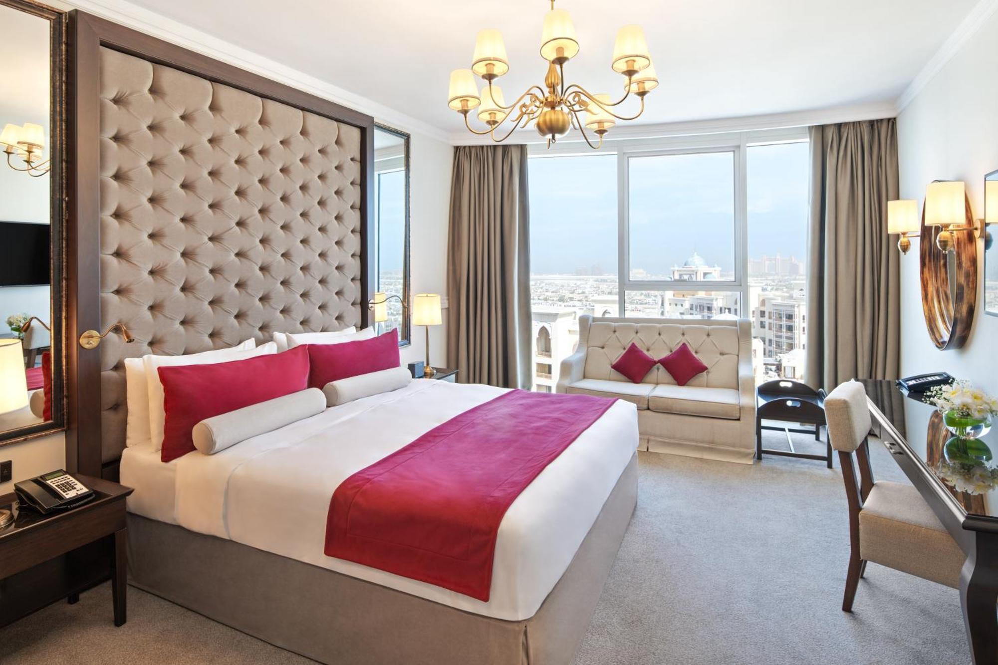 Dukes The Palm, A Royal Hideaway Hotel Dubai Exterior photo The photo shows a luxurious hotel room featuring a large, well-made bed with a plush headboard. The bed is adorned with decorative cushions, primarily in shades of red. There is a stylish sofa nearby, also featuring similar color accents. The room is