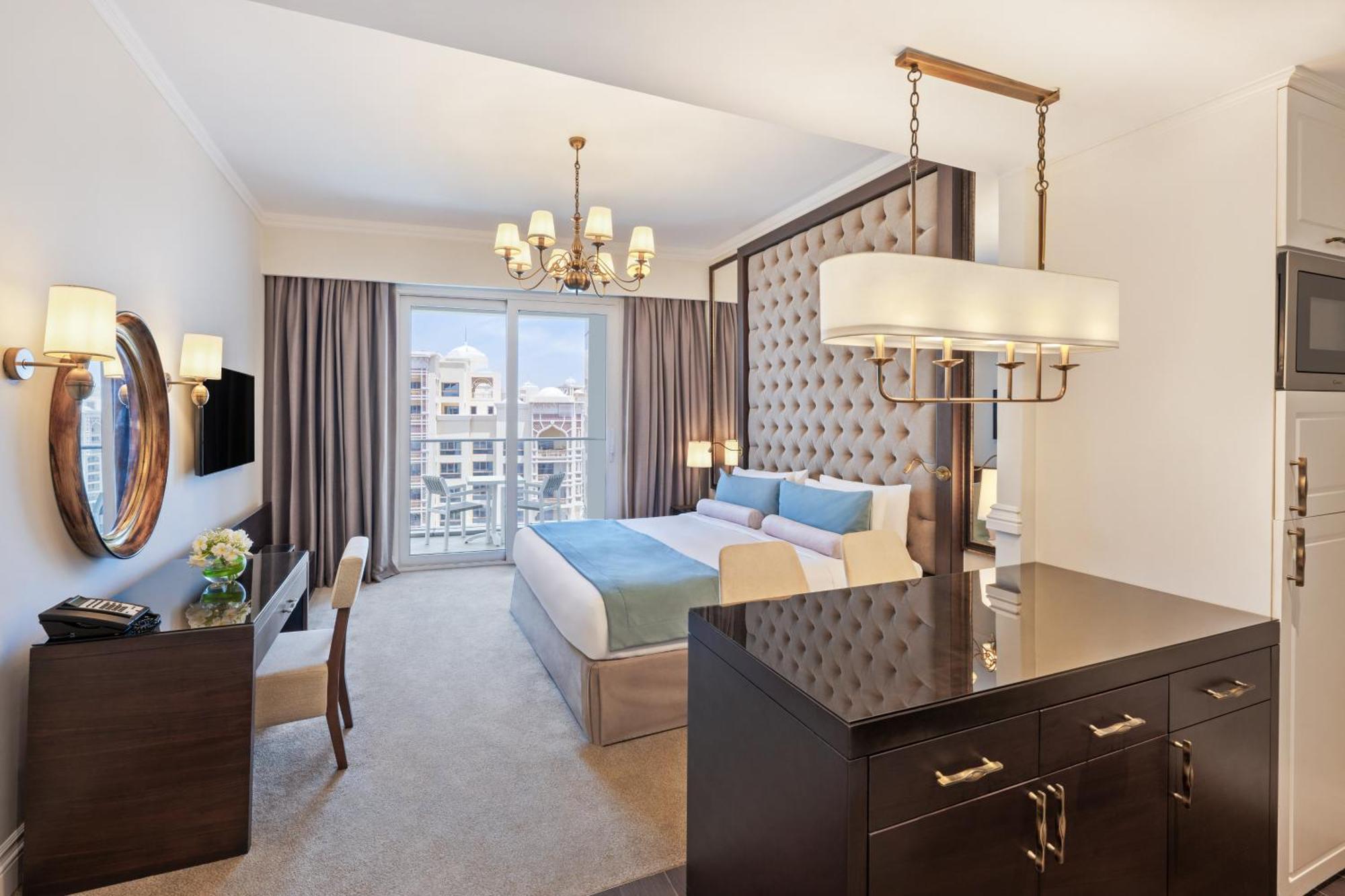 Dukes The Palm, A Royal Hideaway Hotel Dubai Exterior photo The photo shows a luxurious hotel room featuring modern decor. The room includes a large bed with a tufted headboard, soft bedding in light colors, and stylish furnishings. There is a desk and a chair in one corner, along with a decorative mirror and