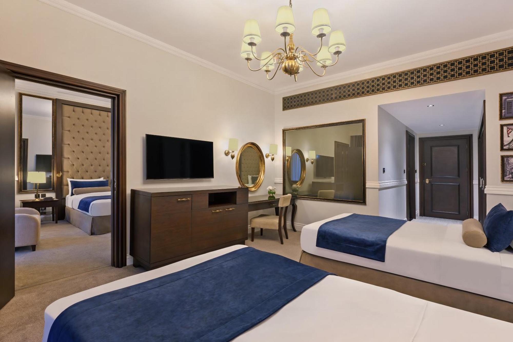 Dukes The Palm, A Royal Hideaway Hotel Dubai Exterior photo The photo shows a hotel room featuring two beds with blue and white bedding. There’s a light-colored carpet on the floor. A chandelier hangs from the ceiling, providing illumination. A wooden dresser is positioned against one wall, with a flat-screen