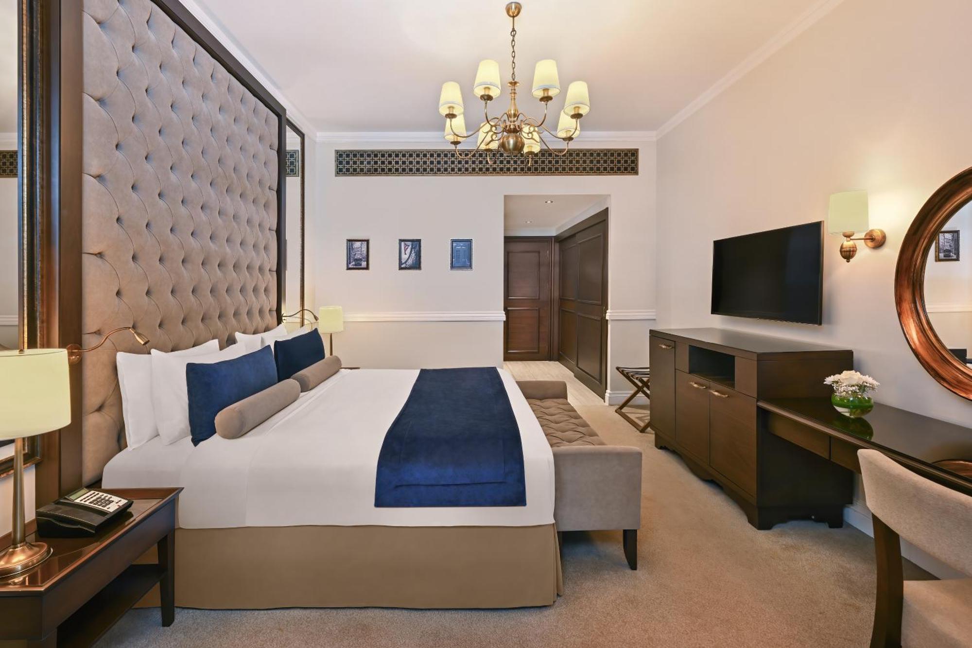 Dukes The Palm, A Royal Hideaway Hotel Dubai Exterior photo The image shows a hotel room featuring a large, neatly arranged bed with decorative pillows. The headboard is tufted and upholstered in a beige fabric. There is a small sofa or bench at the foot of the bed in a contrasting color. The room is well-lit