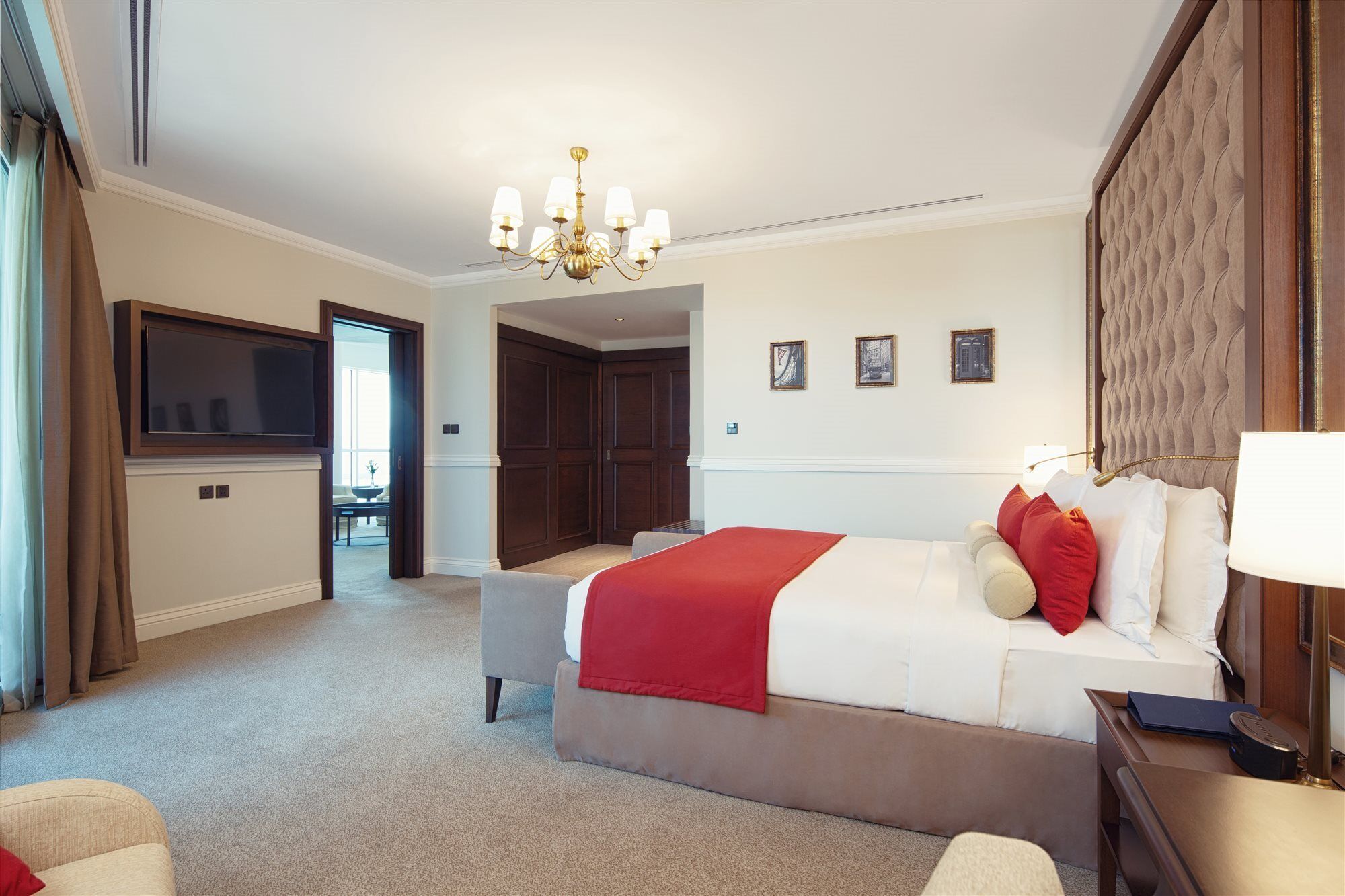 Dukes The Palm, A Royal Hideaway Hotel Dubai Exterior photo The photo shows a well-appointed hotel room. It features a large bed with white linens and red accent pillows. There is a comfortable seating area with a chair, and a side table. A chandelier hangs from the ceiling, providing lighting. On the wall be
