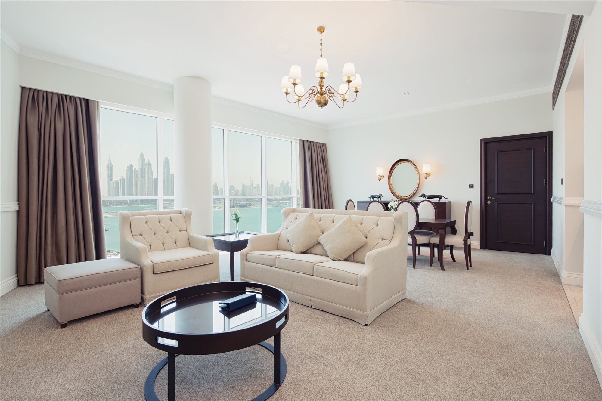 Dukes The Palm, A Royal Hideaway Hotel Dubai Exterior photo The photo shows a stylish and modern living room. It features a comfortable light-colored sofa with decorative cushions, a round black coffee table in the center, and a small matching stool nearby. There are large windows with views of a city skyline
